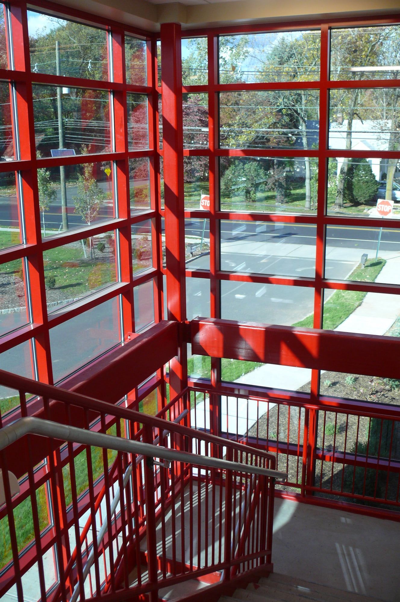Stairwell with a red metal frame and railings overlooking a street through large, glass-paned windows.