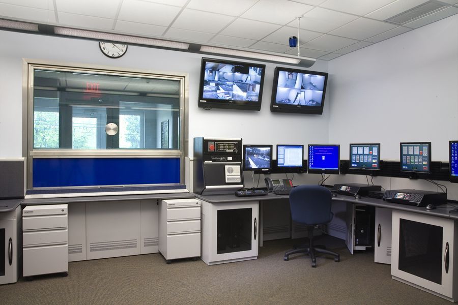 Security control room featuring multiple computer monitors, surveillance screens, and desks in a professional office.