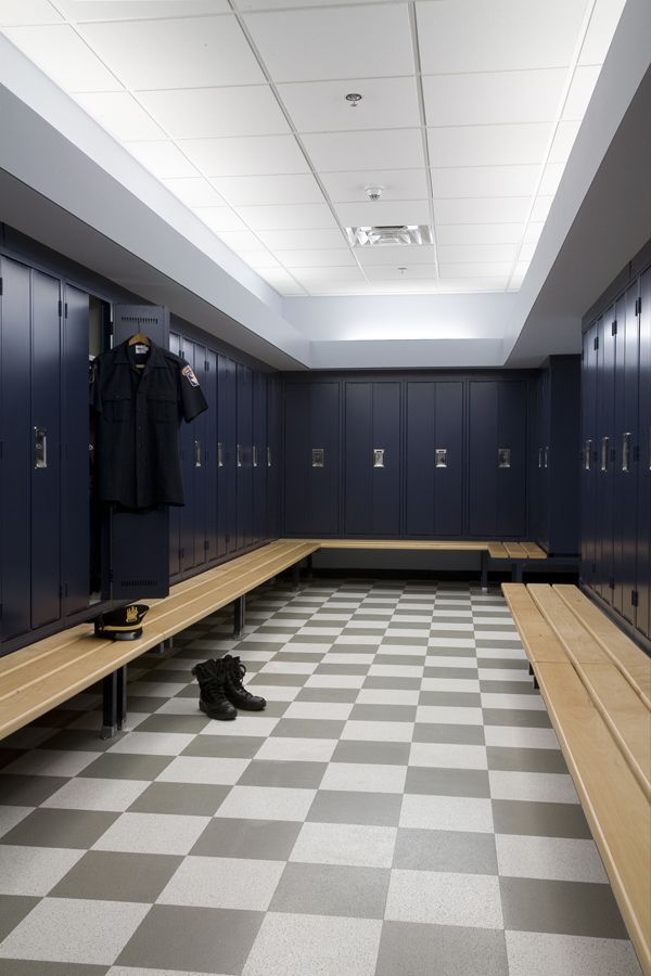 An empty locker room with dark blue lockers, wooden benches, and a gray and white checkered floor.