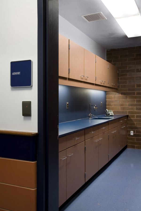 A view through a doorway into a sterile lab space with brown cabinets, a dark blue countertop, sink, and brick wall.