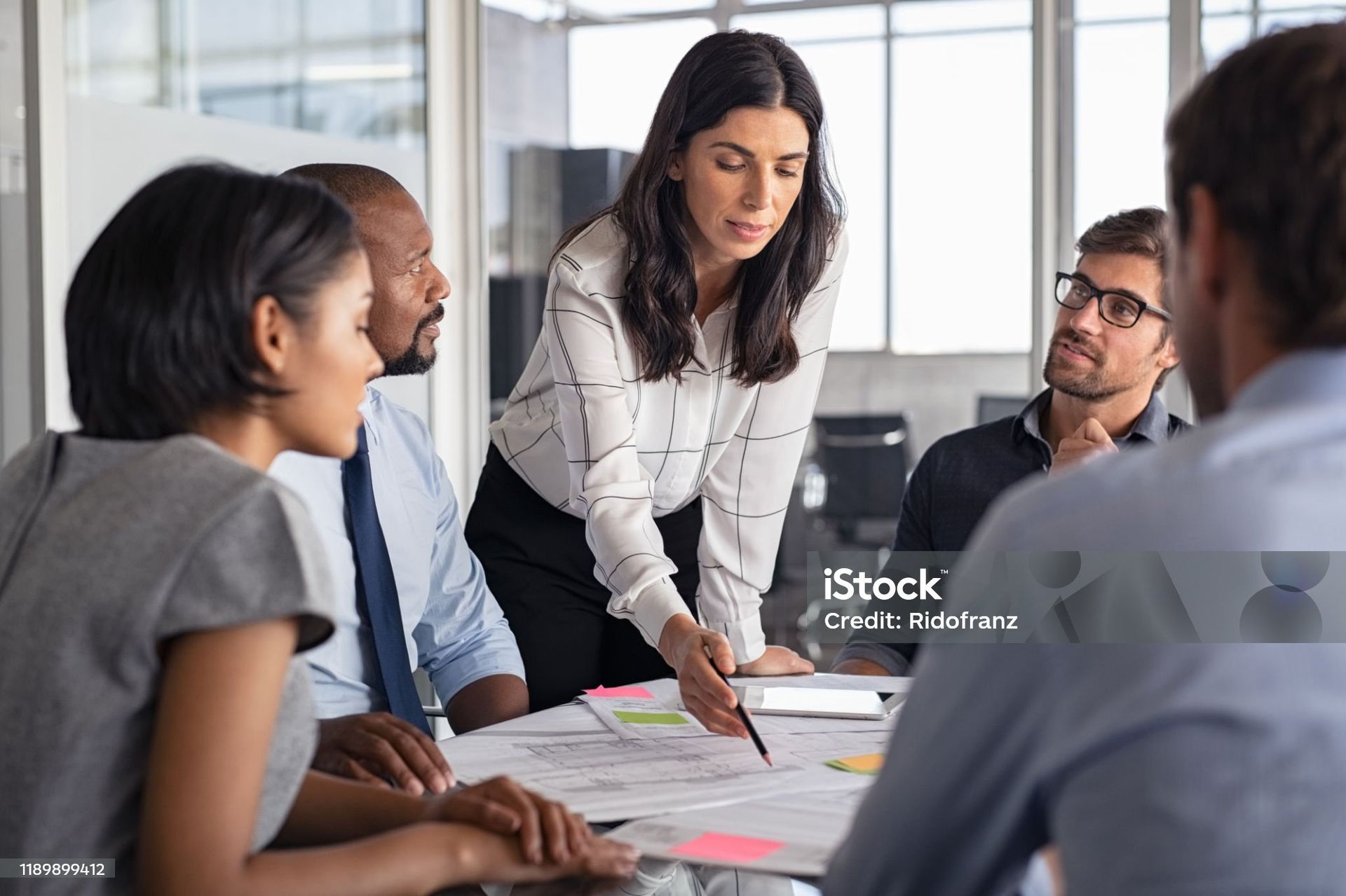 A group of colleagues in a bright office consults documents on a table as a professional points to a paper.