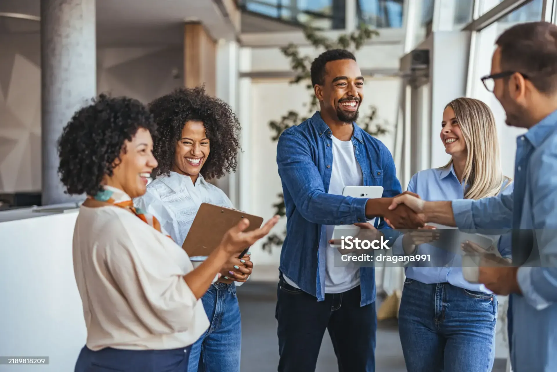 Colleagues in an office setting shake hands and smile while conversing, creating a professional and friendly atmosphere.