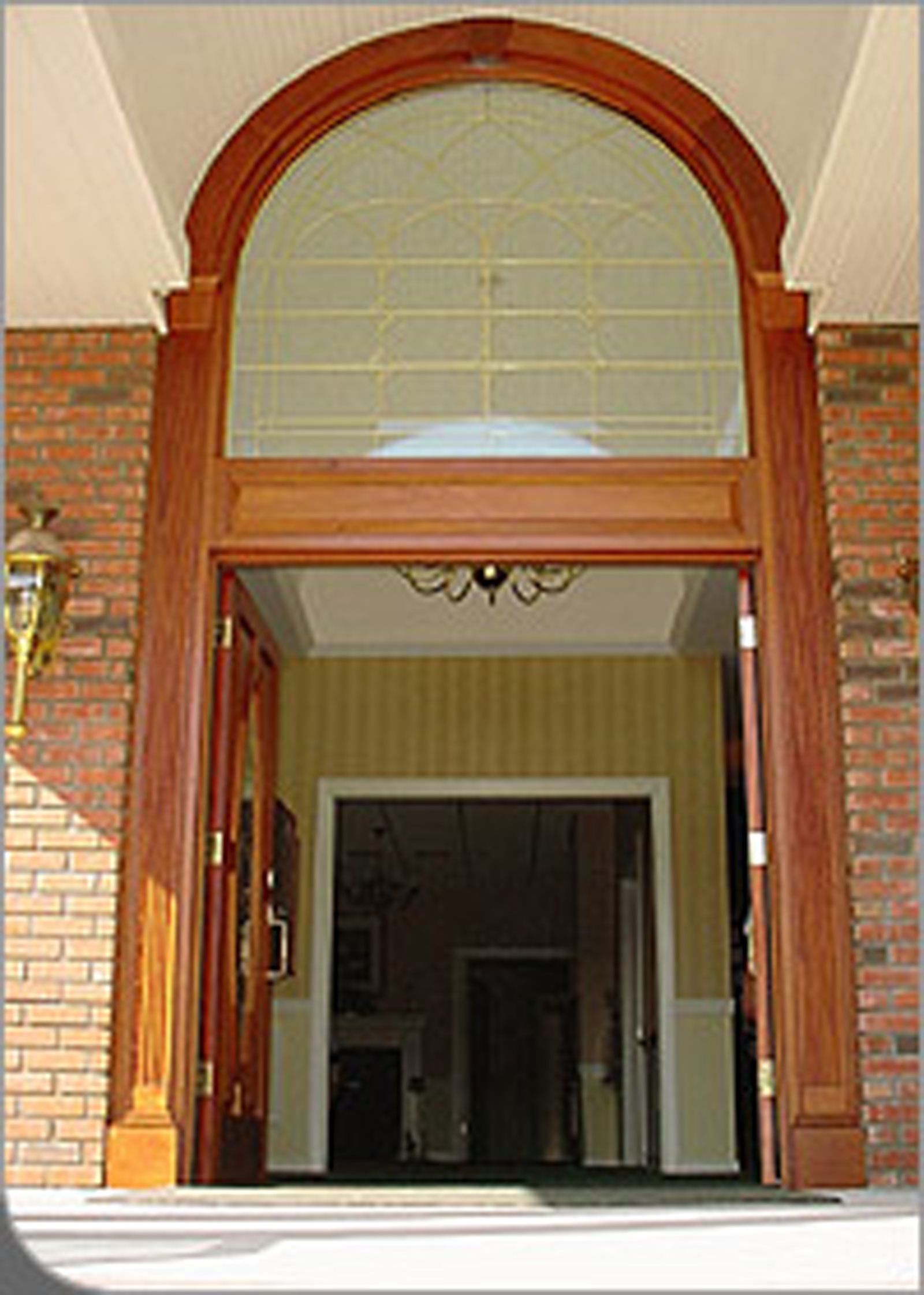 A grand wooden entryway featuring an arched glass transom window above open doors, set against a red brick exterior.