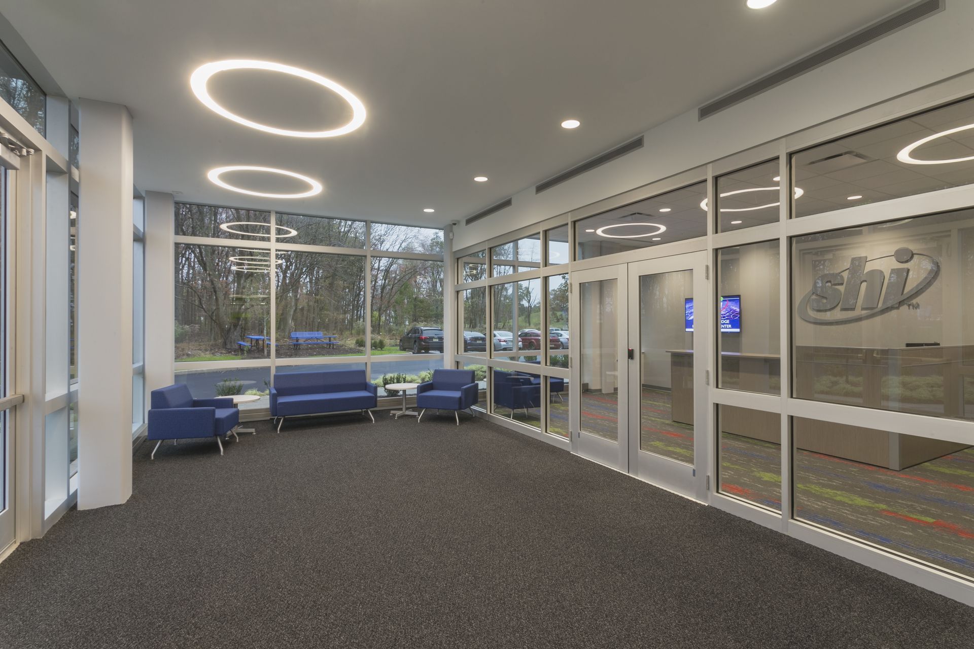 Modern office lobby with a glass wall, blue seating area, and the SHI logo on the glass entrance door.