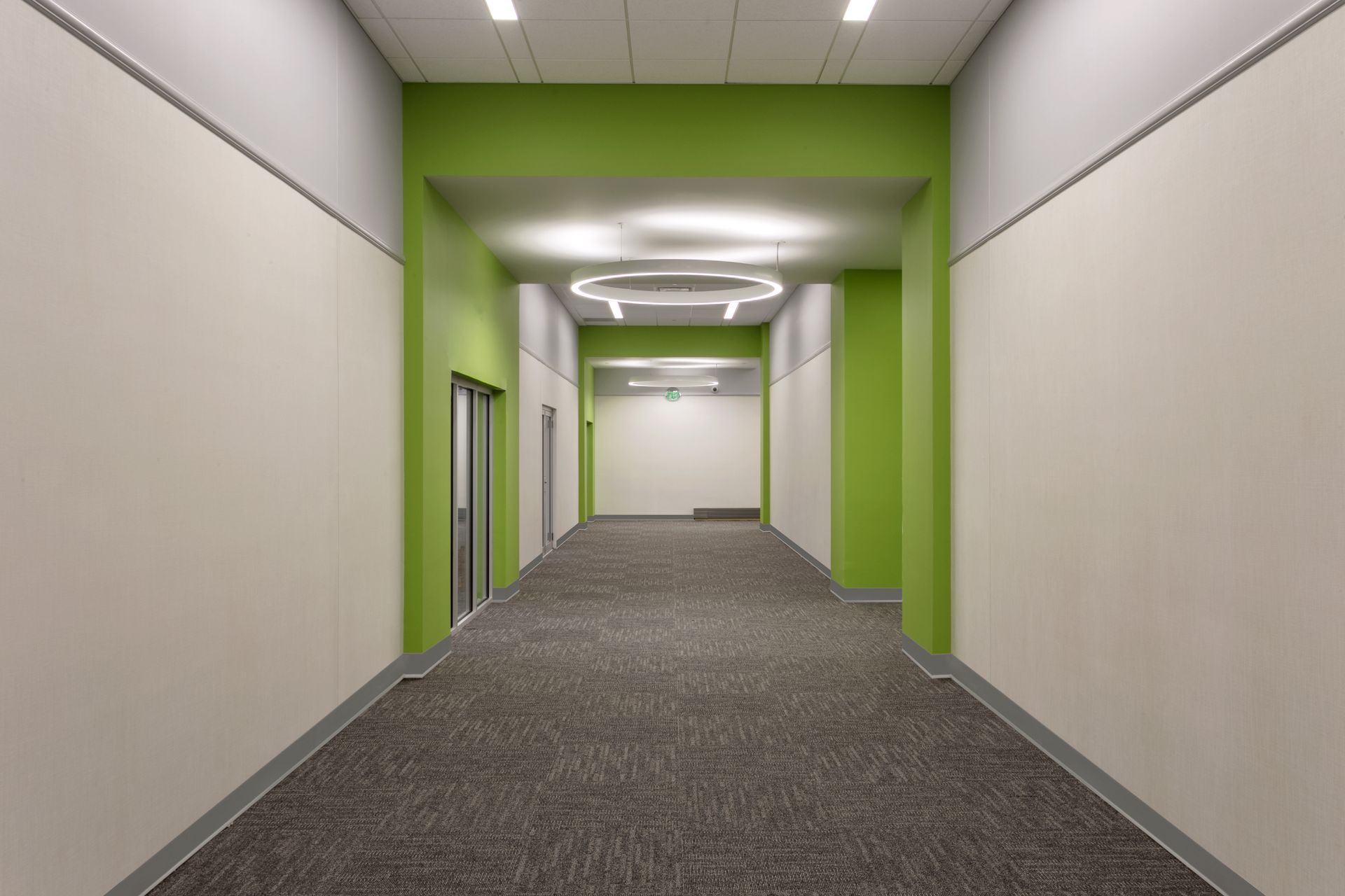 A long, empty indoor hallway with gray carpet, light beige walls, and bright green accent walls.
