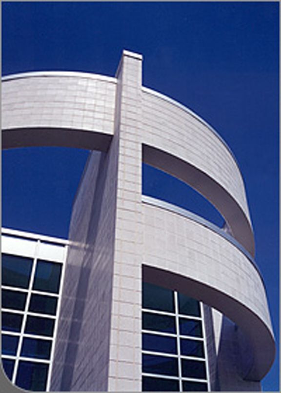 Modern two-story brick building with red-framed windows and doors under a blue sky with clouds.