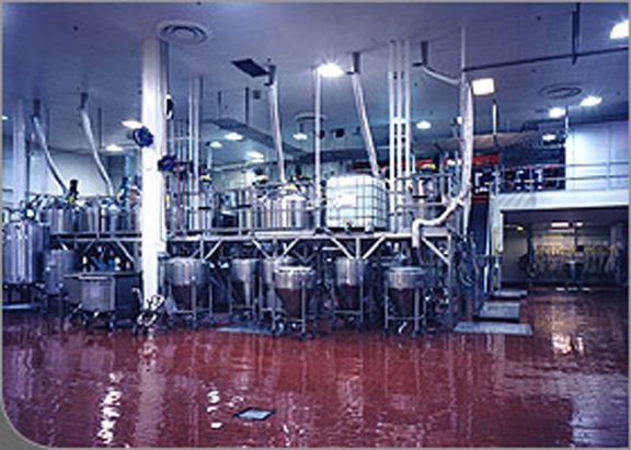 Industrial food processing facility featuring large stainless steel mixing tanks and piping on a dark red floor.