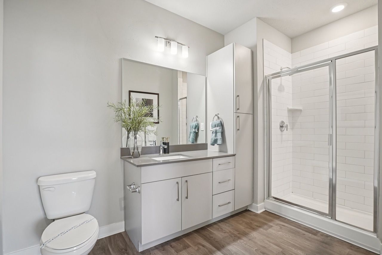 Modern apartment bathroom with vanity, mirror, storage cabinet, and glass-enclosed shower.