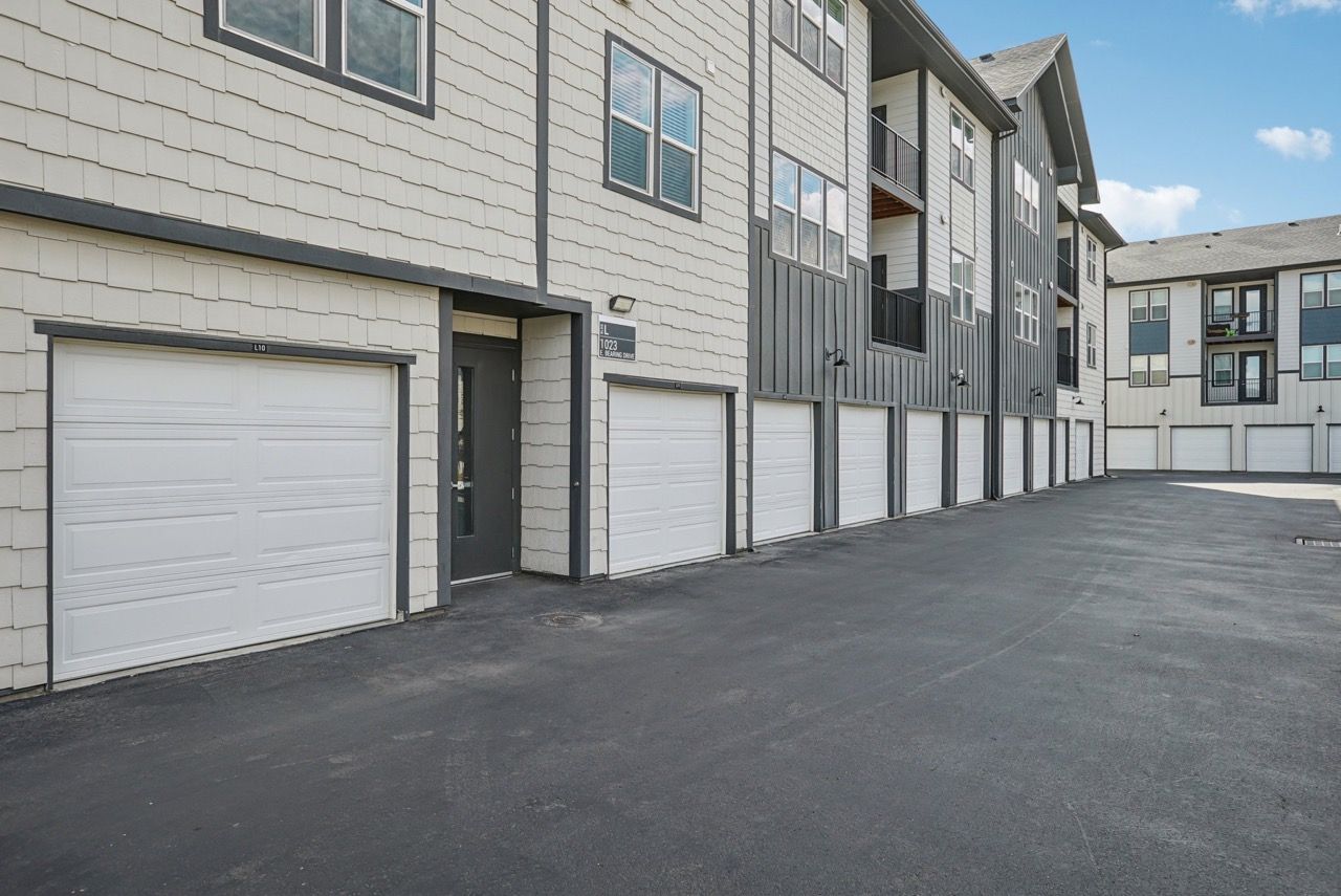 Exterior view of a modern multifamily building with row of attached garages along a paved driveway.