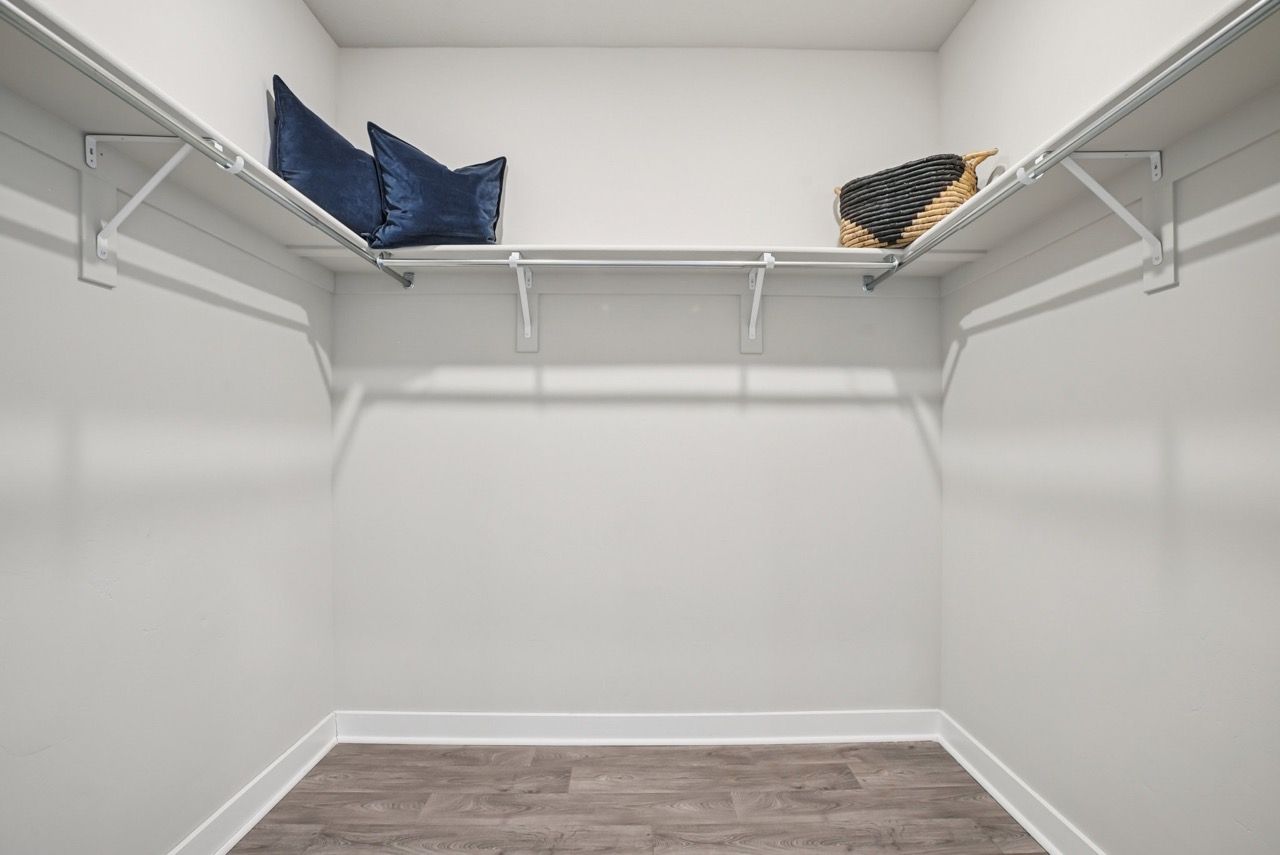 Walk-in closet with white walls, metal hanging rods, shelves, and a woven basket on the top shelf.