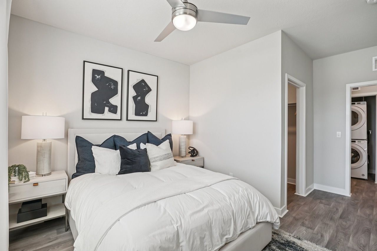 Bedroom with white bedding, navy pillows, two nightstands, lamps, and a ceiling fan.