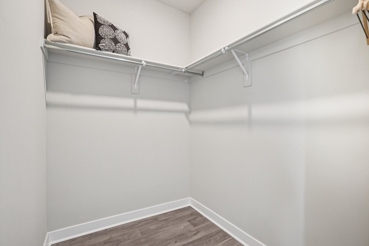 Empty walk-in closet with double hanging rods and a top shelf.