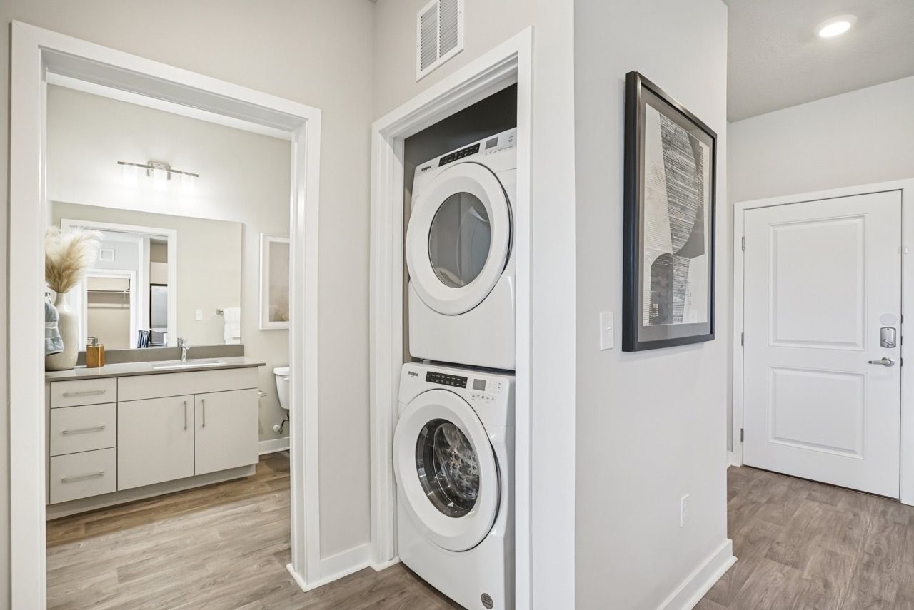 In-unit laundry closet with stacked washer and dryer beside hallway and bathroom vanity.