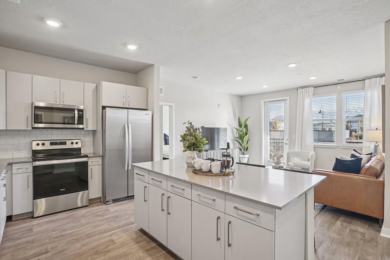 Open-concept kitchen with white cabinets, stainless steel appliances, and adjacent living area.