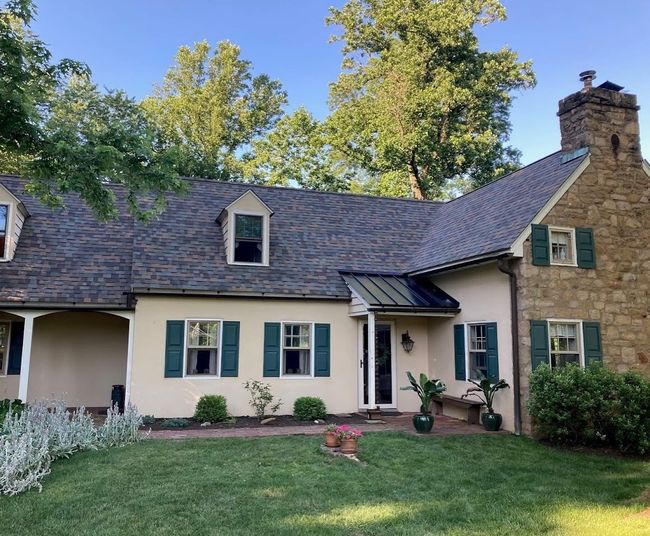 A yellow house with green shutters and a stone chimney