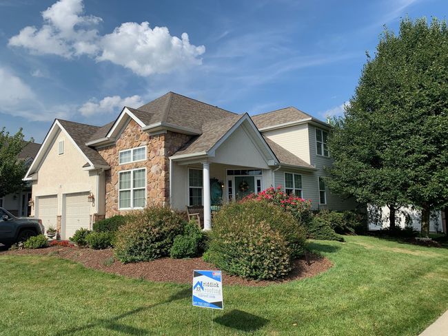 A large house with a Riddick Roofing yard sign in front of it.