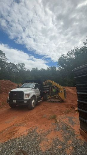 A white truck is parked next to a bulldozer on a dirt road.