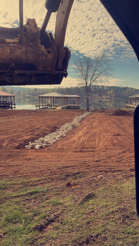 Excavation equipment moving dirt in a field near a lake.