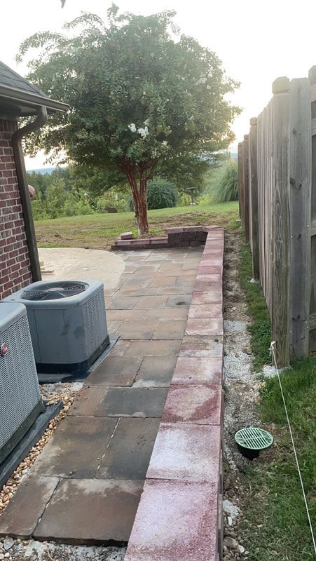 A brick walkway leading to a fence with a tree in the background.