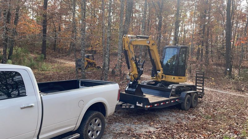 A white truck is towing a small excavator on a trailer.