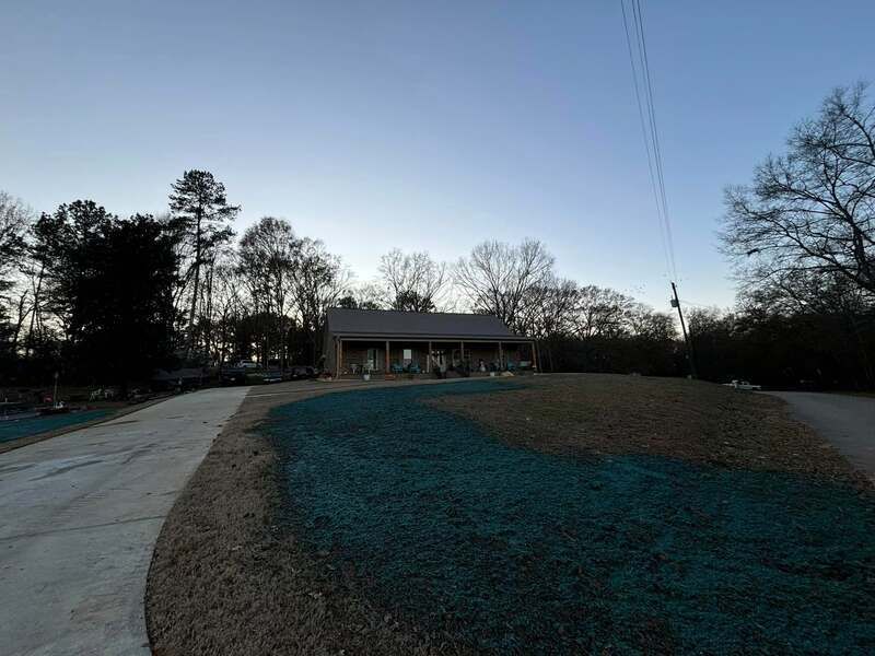 A house with a driveway leading to it and trees in the background.