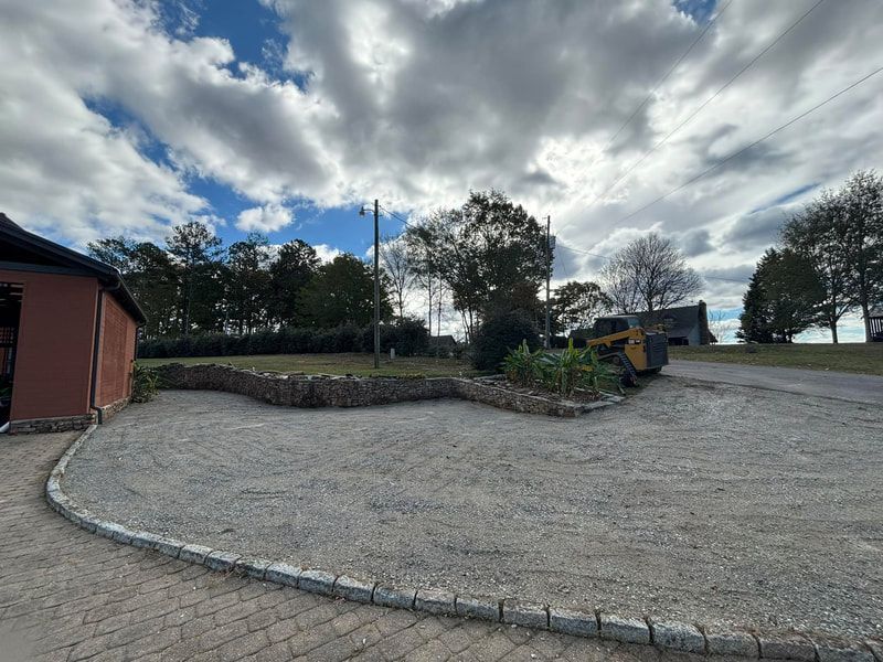 A tractor is parked in a gravel driveway in front of a house.