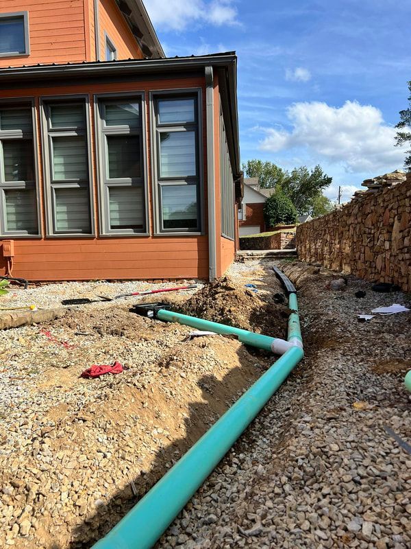 A green pipe is laying in the dirt in front of a house