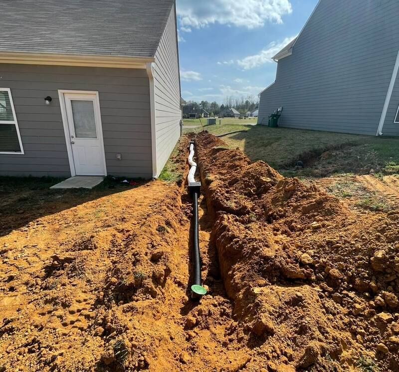 A pipe is being installed in the dirt in front of a house.