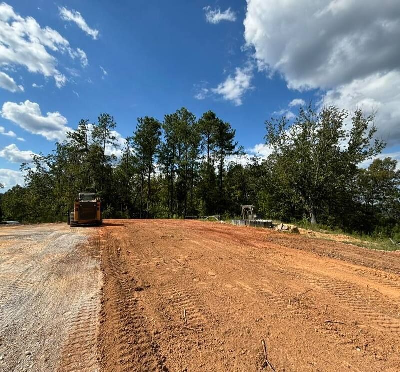 Excavation equipment is driving down a dirt road with trees in the background