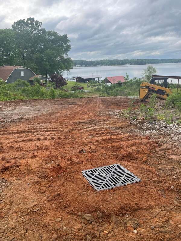 A drain cover is sitting in the middle of a dirt road next to a lake.