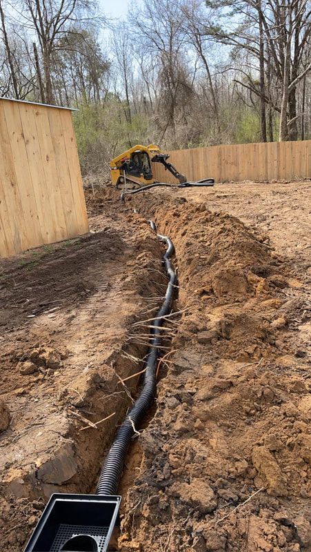 A drain pipe is being installed in the dirt next to a wooden fence.