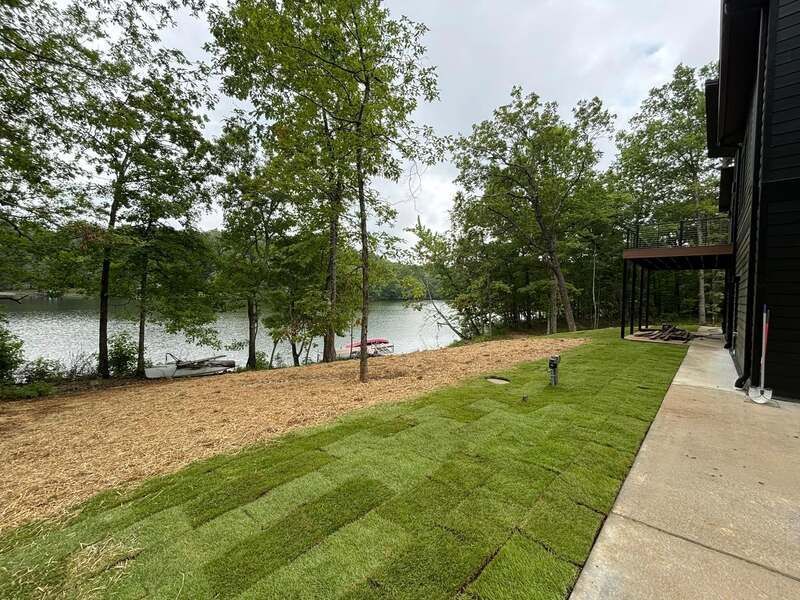 A large lawn with a lake in the background and a boat in the water.