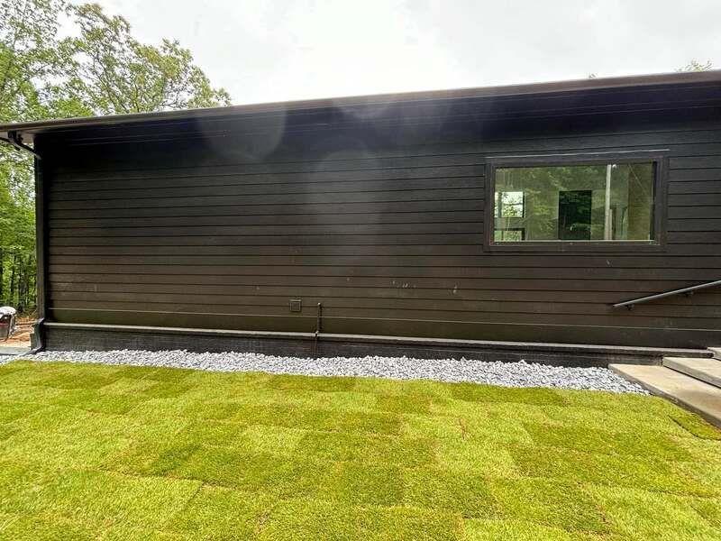A black house with a lush green lawn in front of it.