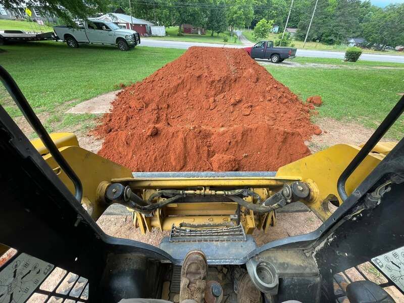 Excavation equipment is moving a pile of dirt in a yard.