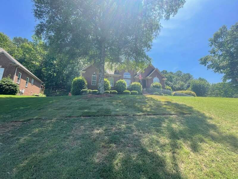 A large brick house sits on top of a lush green hillside surrounded by trees.