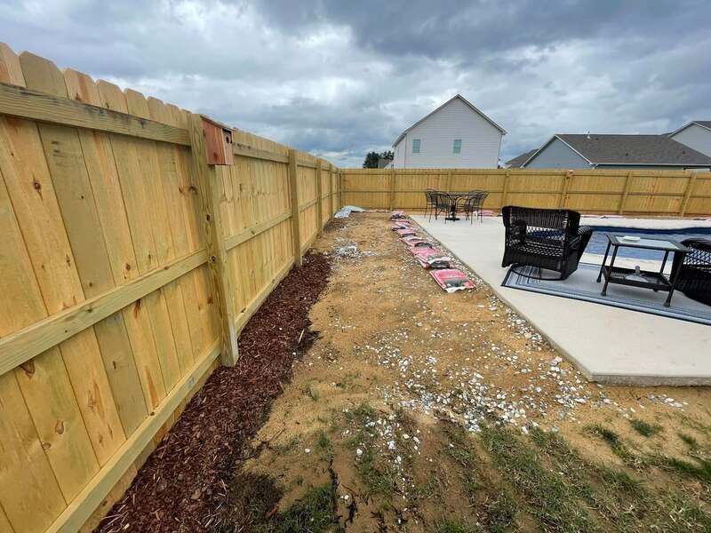 A wooden fence surrounds a patio area in a backyard.