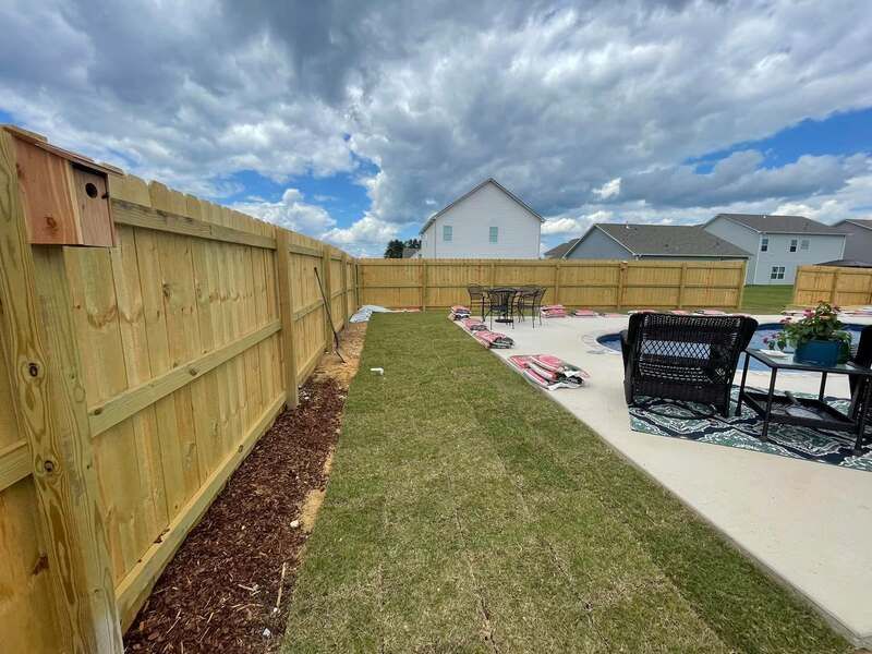 A wooden fence surrounds a backyard with a patio and chairs.