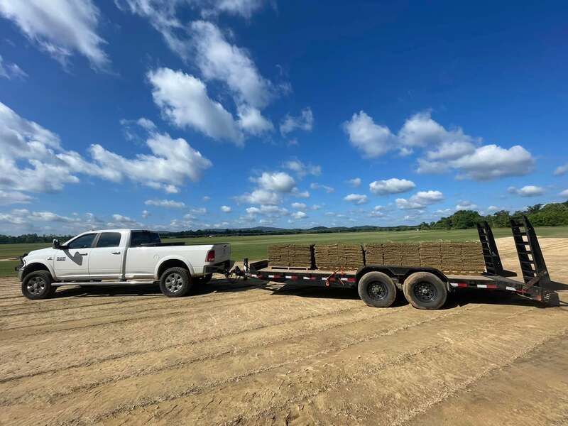 A white truck is towing a trailer filled with hay.