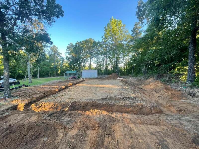 A dirt field with trees in the background and a building in the background.