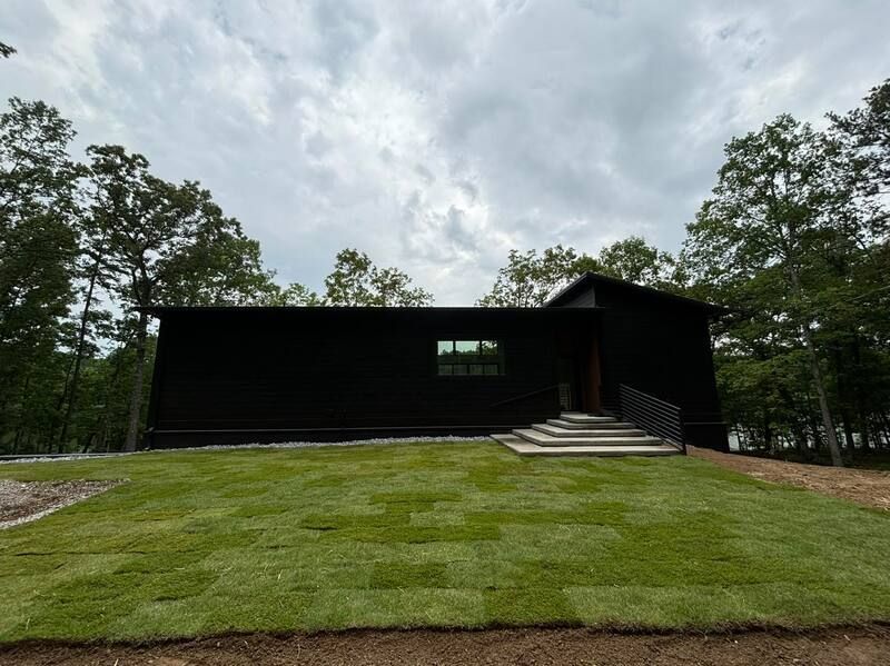 A black house is sitting on top of a lush green hill surrounded by trees.