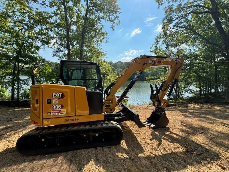 A yellow cat excavator is parked in a dirt field near a lake.