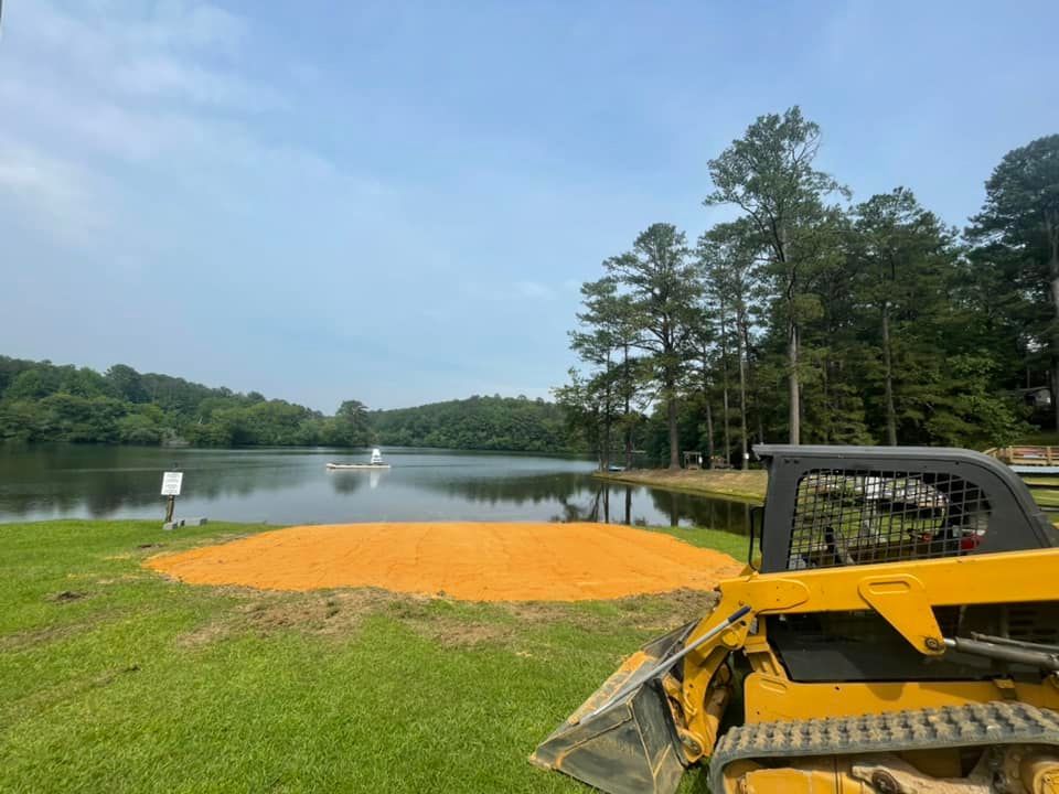 Excavation equipment sitting on the grass next to a lake.