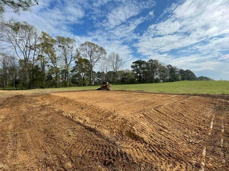 Excavation equipment is moving dirt in a field with trees in the background.