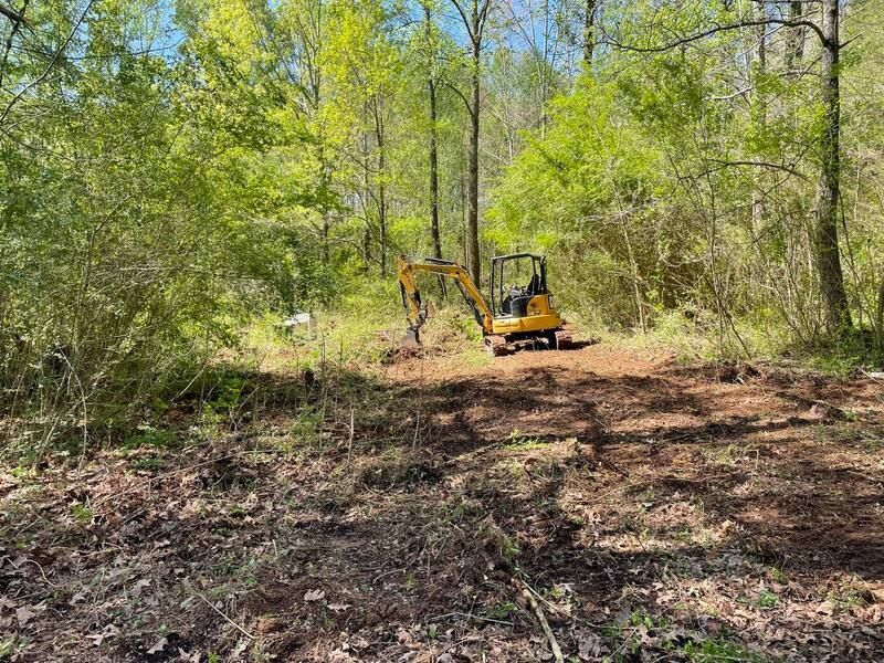 A yellow excavator is working in the middle of a forest.