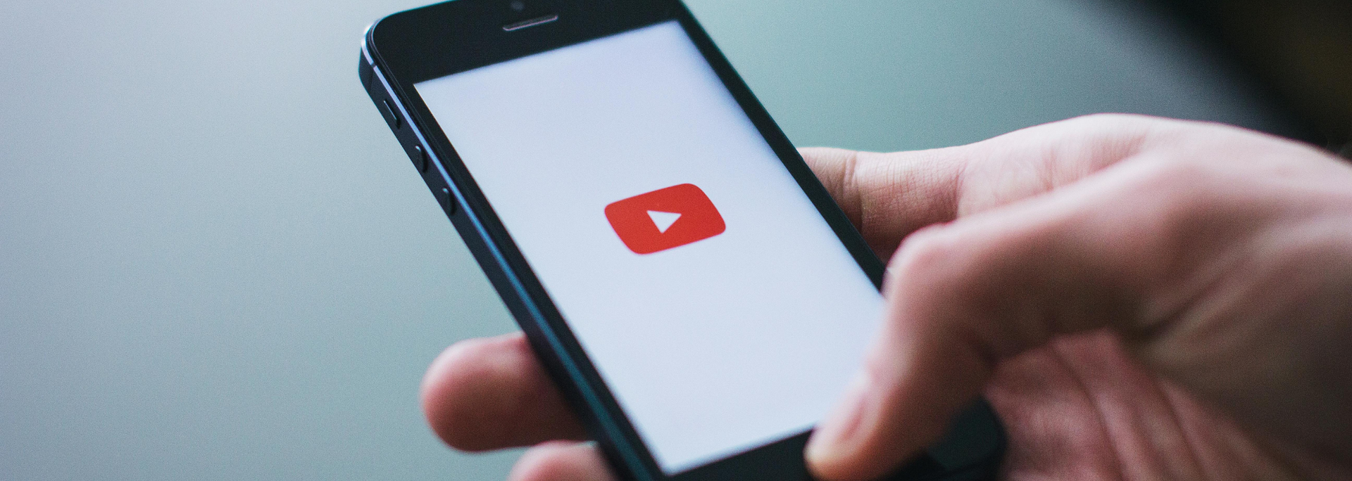 Hand holding a smartphone displaying the YouTube play icon on a white screen