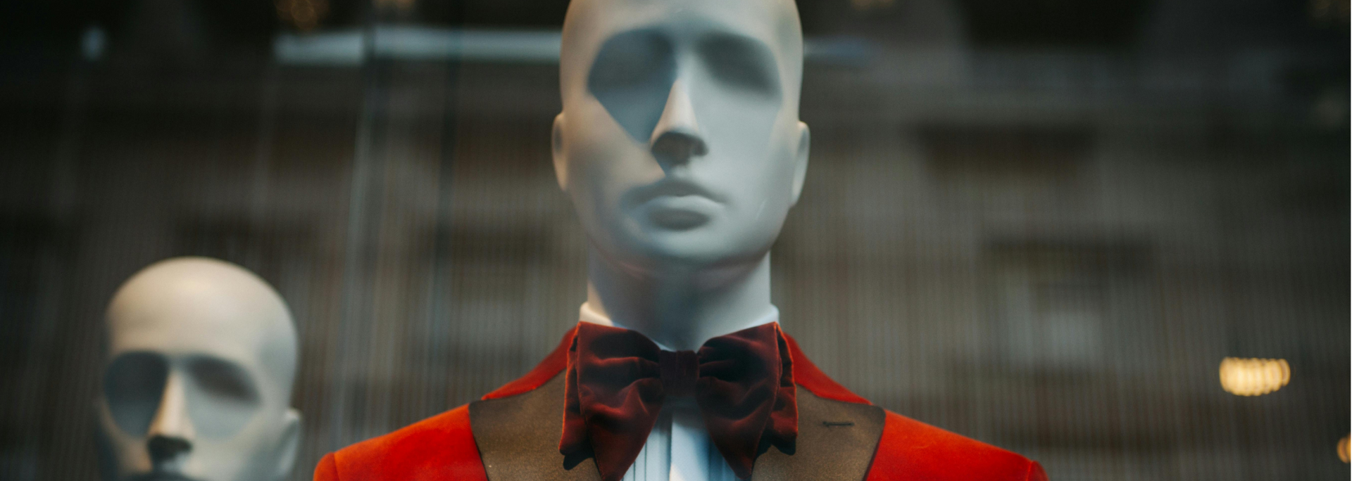 Mannequins in red jackets and black bow ties displayed behind glass in a storefront window