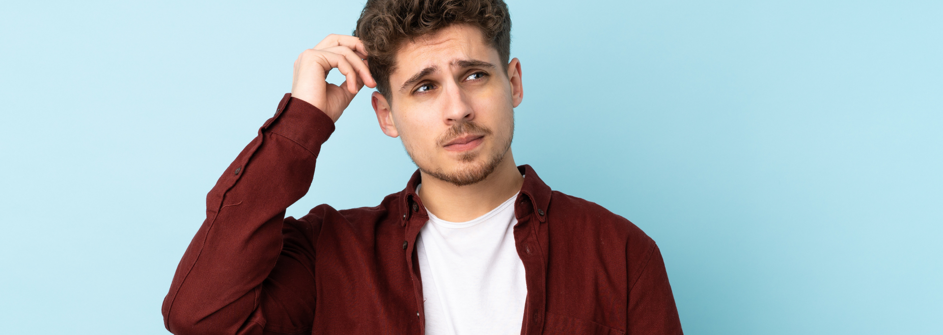 Young person in a maroon shirt scratching their head against a light blue background