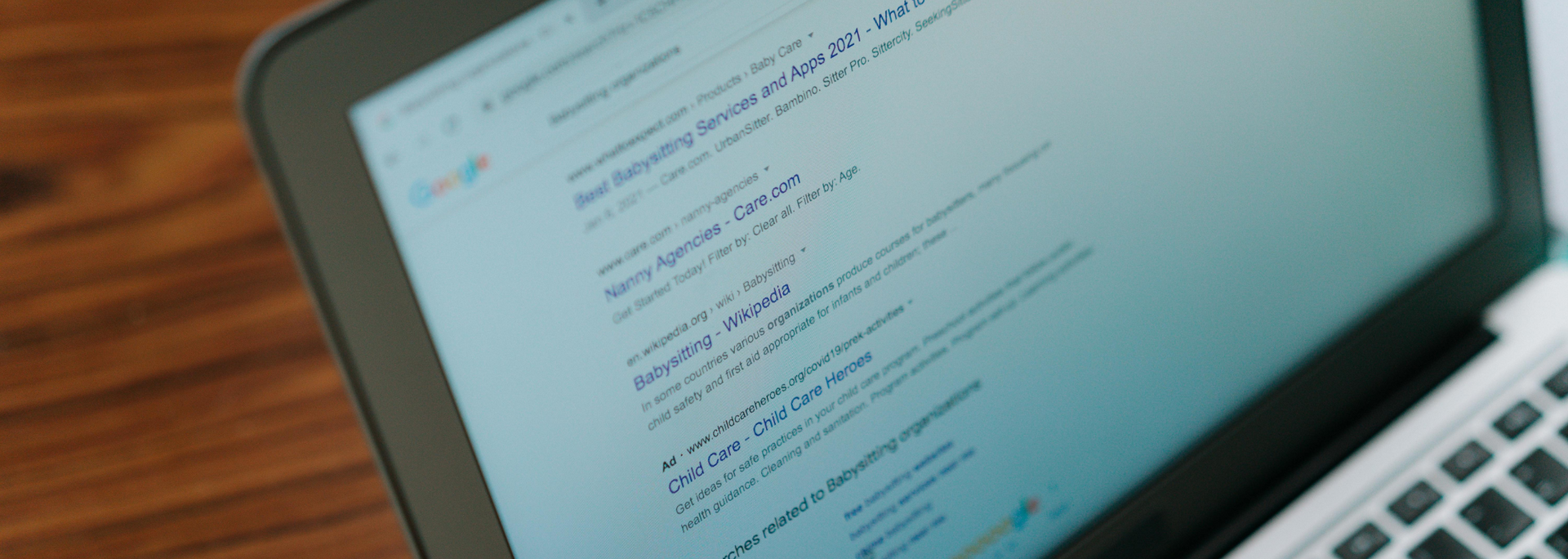 Laptop screen showing code or text on a white webpage, viewed at an angle on a wooden table.