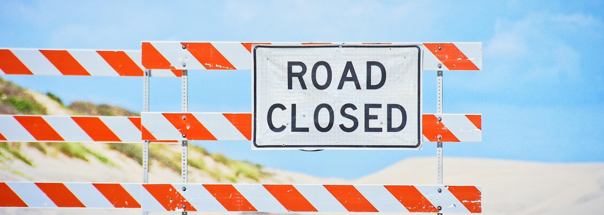 Road closed sign on orange-and-white striped barricade against a blue sky