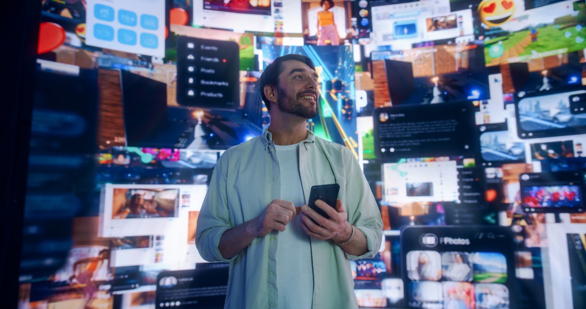 Man standing with a phone in a room of many glowing digital screens and displays